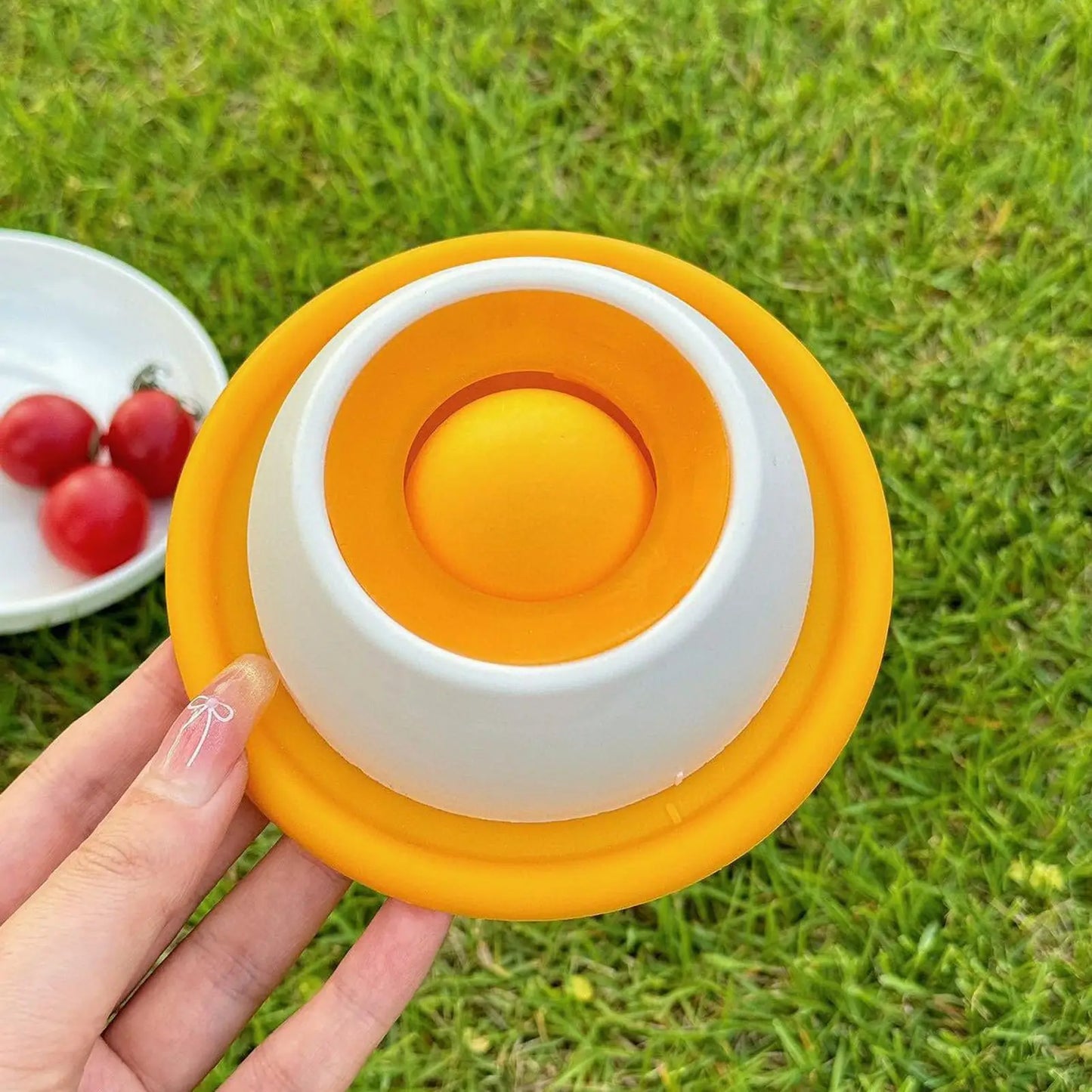 Hand die een oranje-witte PawLuxe Likmat & Slow Feeder voor honden en katten vasthoudt op gras, ontworpen om voedingstijd langzamer en leuker te maken.